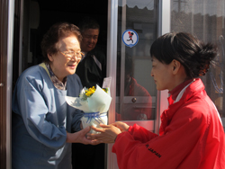 被災者の中村ちや子さんに花とメッセージを渡す事務局の伊藤