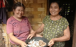 ソーパ・チャンミーさんと母親が、収穫したキノコが入った入れ物を2人で持ち、嬉しそうに微笑む