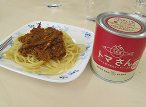 缶詰にはトマさんソースと書かれている。よこにはパスタがお皿にのっていて、そのうえには赤いソースがかけられている
