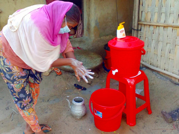 蛇口があり水が入った赤いポリタンクの前で、ソープを使い手洗い方法を女性が実演している