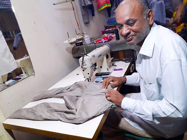ミシン台に男性が座り、ズボンの生地を縫う作業をしている