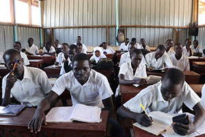 数十名の生徒が教室でノートやペンを手に勉強している　どの生徒も白い半そでの制服を着ている