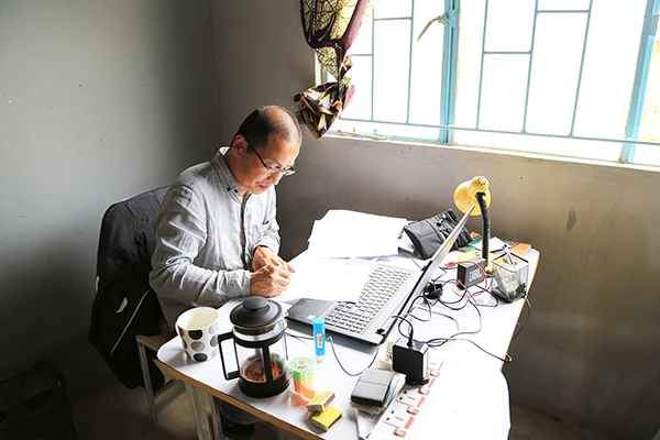 事務所デスクにつく直江さん。ペンを持ち紙に何かを書いている。静謐な雰囲気が伝わってくる