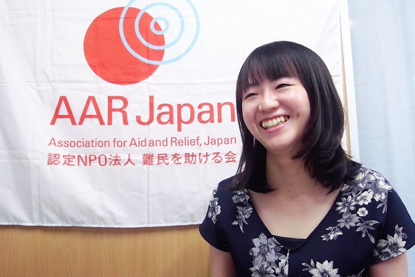 AARのロゴ入り旗をバックに、笑顔で話す藤田