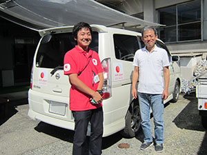 AARが提供した送迎用の車両の前に立つ施設長の森慶一さんとAARの高木卓美
