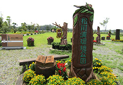 松川浦環境公園と書かれた木彫りの大きな看板（モニュメント）。その周辺には色鮮やかな花が咲き誇っている
