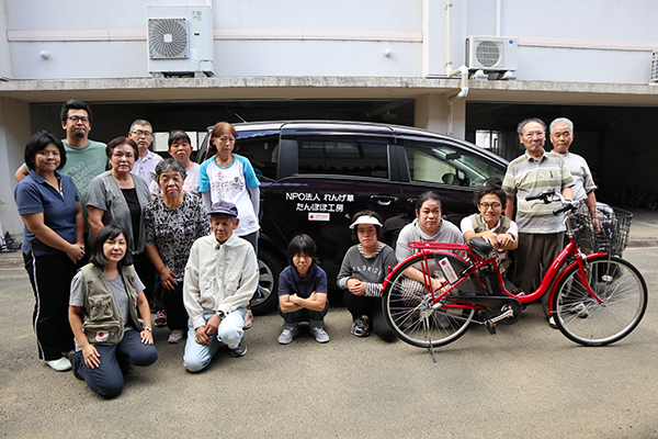 提供した車と自転車と一緒に、れんげ草の方13名、AARスタッフ2名で記念撮影