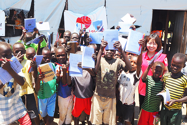 10数名の子どもたちが集まり、受け取ったノートと鉛筆を頭上に挙げている様子