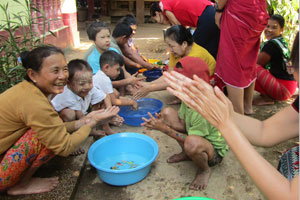 約10人の子どもたちや大人が手を合わせて、手洗いの練習を行う。バケツには水が入り、参加者はバケツを囲みしゃがんでいる。
