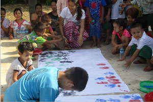 子どもたちが赤や青や緑の絵の具を手のひらに塗り、一枚の白い大きな布に手形を押す