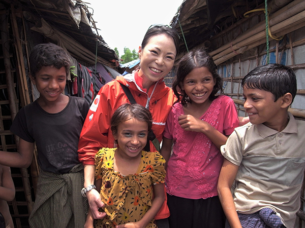 難民キャンプの中で4名の笑顔の子どもに日本人女性が囲まれている