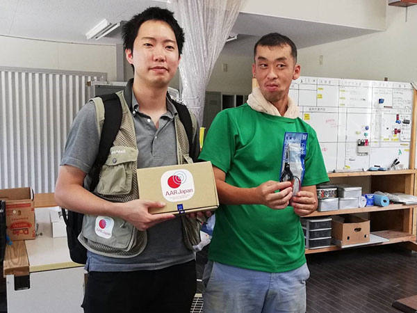 福祉施設を利用される男性とAARの生田目が、AARが寄付をしたハサミとハサミが入った箱を持っている