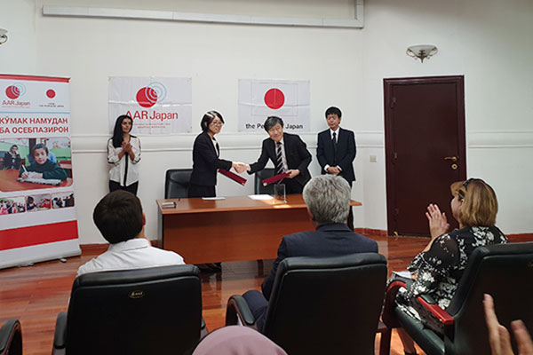 署名式では、日本大使館の職員とAAR山根がスーツを着て、握手を交わしている。関係者はイスに座った状態で拍手を送っている