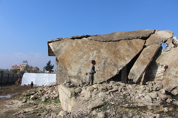 砲撃によって崩壊し、放置された建物の前で少年が佇んでいる