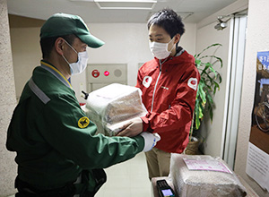 AAR緊急支援チームの生田目が、配送業者にマスクなどの支援物資が入ったダンボールを手渡している