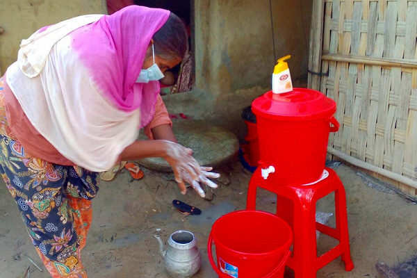 女性が赤い蛇口がついたポリバケツの前で、手を洗っている。手にはソープの泡がついている