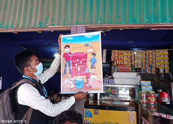 飲料などの日用品が売られている小売店の軒先に、ポスターを掲示する現地協力団体の職員