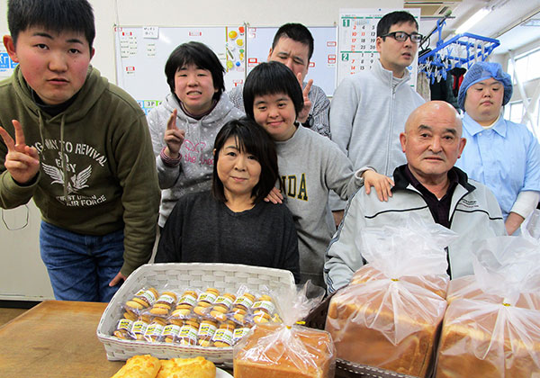 馬場さんと伊藤さん、利用者の方々6名が、製造したパンやクッキーと一緒に写っている