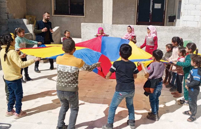 Children in a circle holding a large, colorful piece of cloth