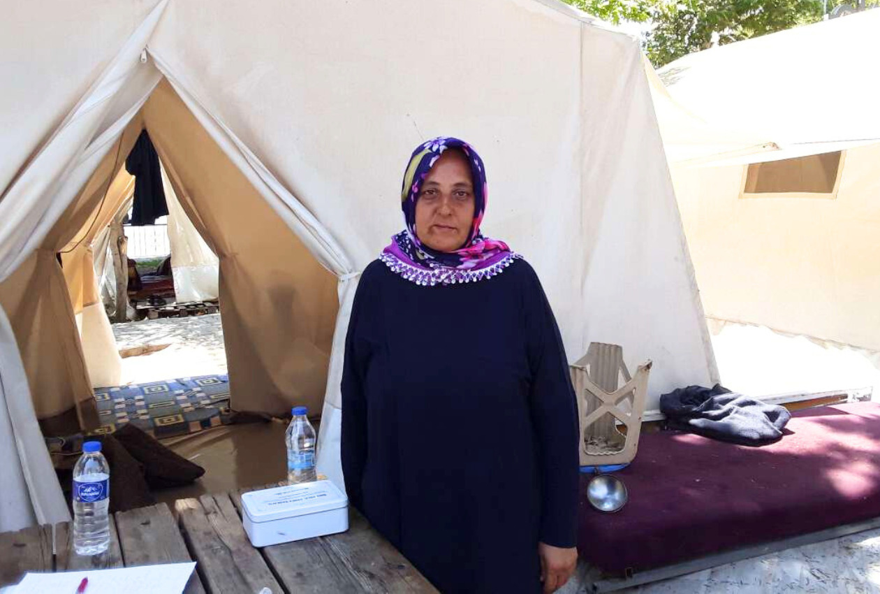 Photo of a female survivor standing in front of her tent