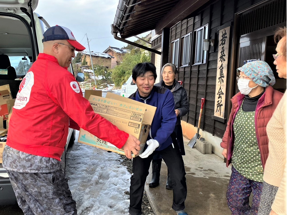 An AAR staff member hands a cardboard box to a man in front of a meeting place.