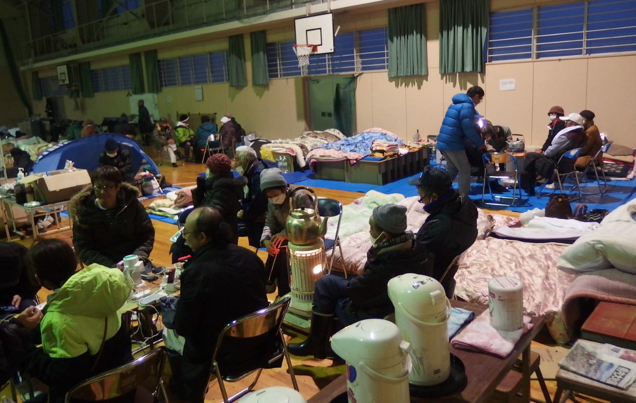 Many evacuees sitting on the floor of school gym.