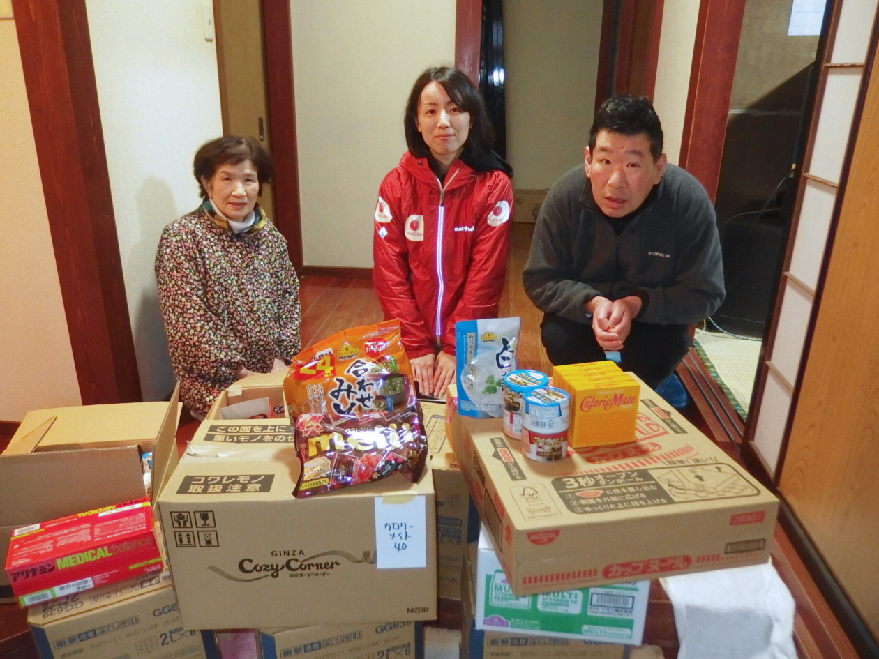 AAR staff member and a man and a woman sitting behind the food and hygiene supplies