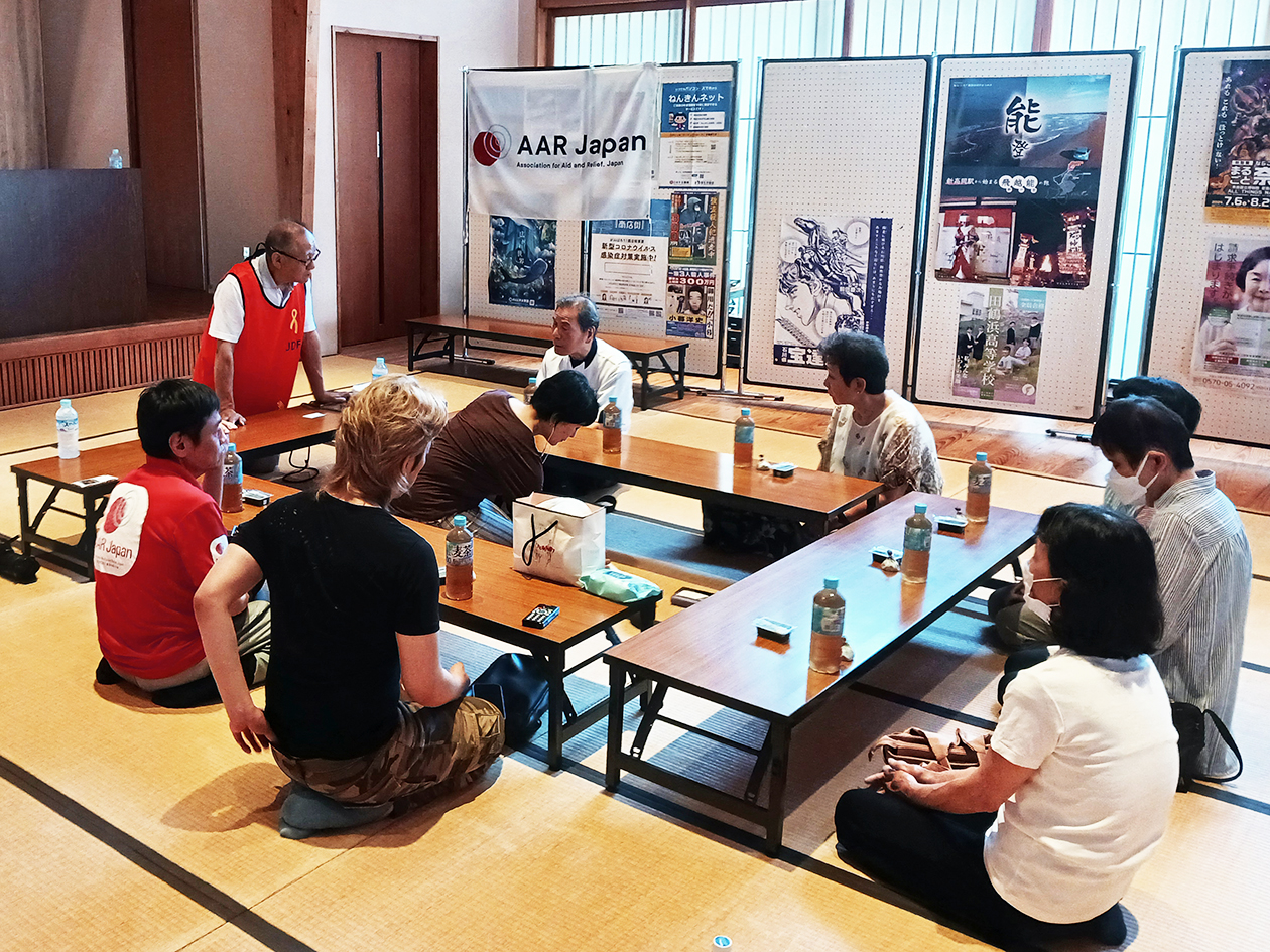 A long desk is placed on a tatami mat, surrounded by about 10 people