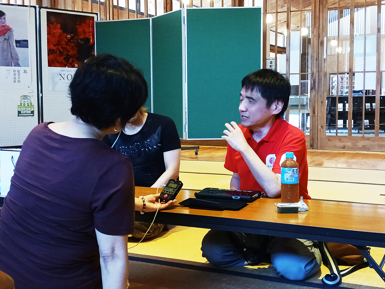 Tamaru, wearing an AAR polo shirt, is talking to a woman across the desk