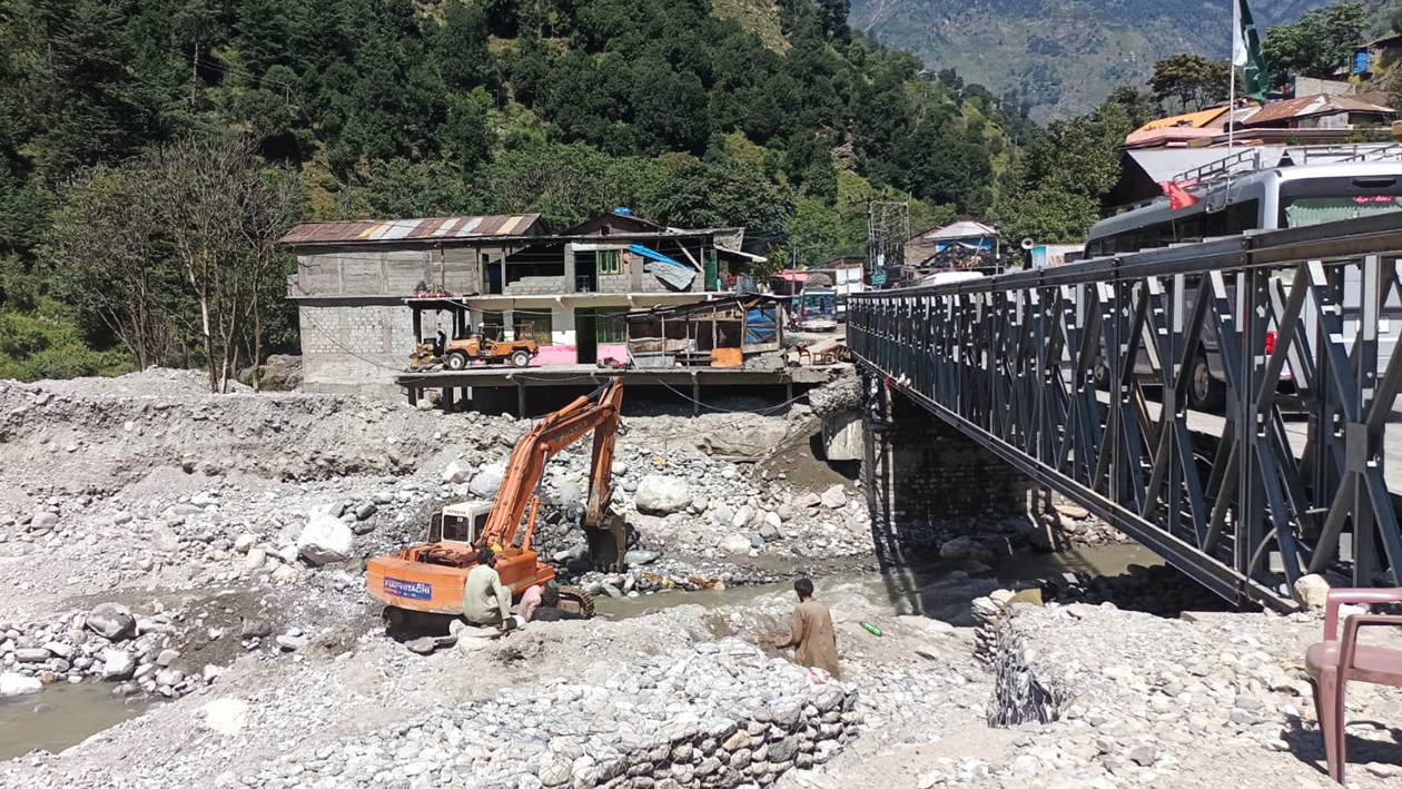 A power shovel is carrying earth and sand under the bridge.