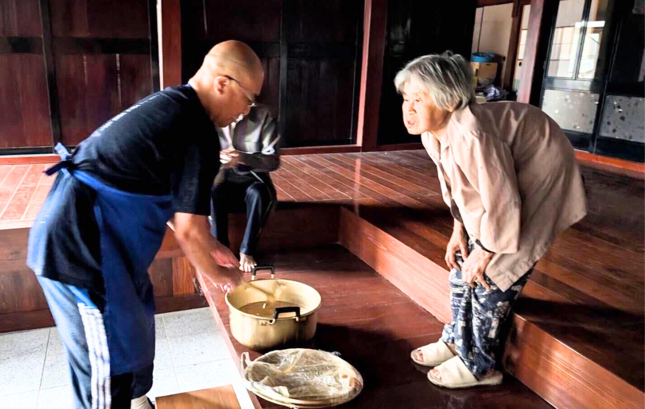 A man handing out food at the entrance and an elderly woman receiving it