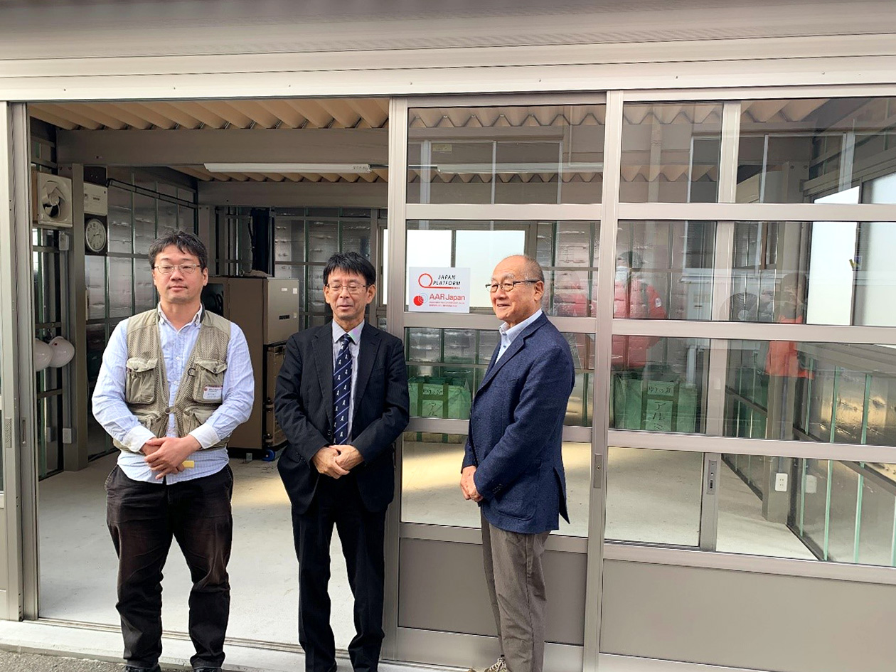 Three men are pictured side by side in front of the one-story facility