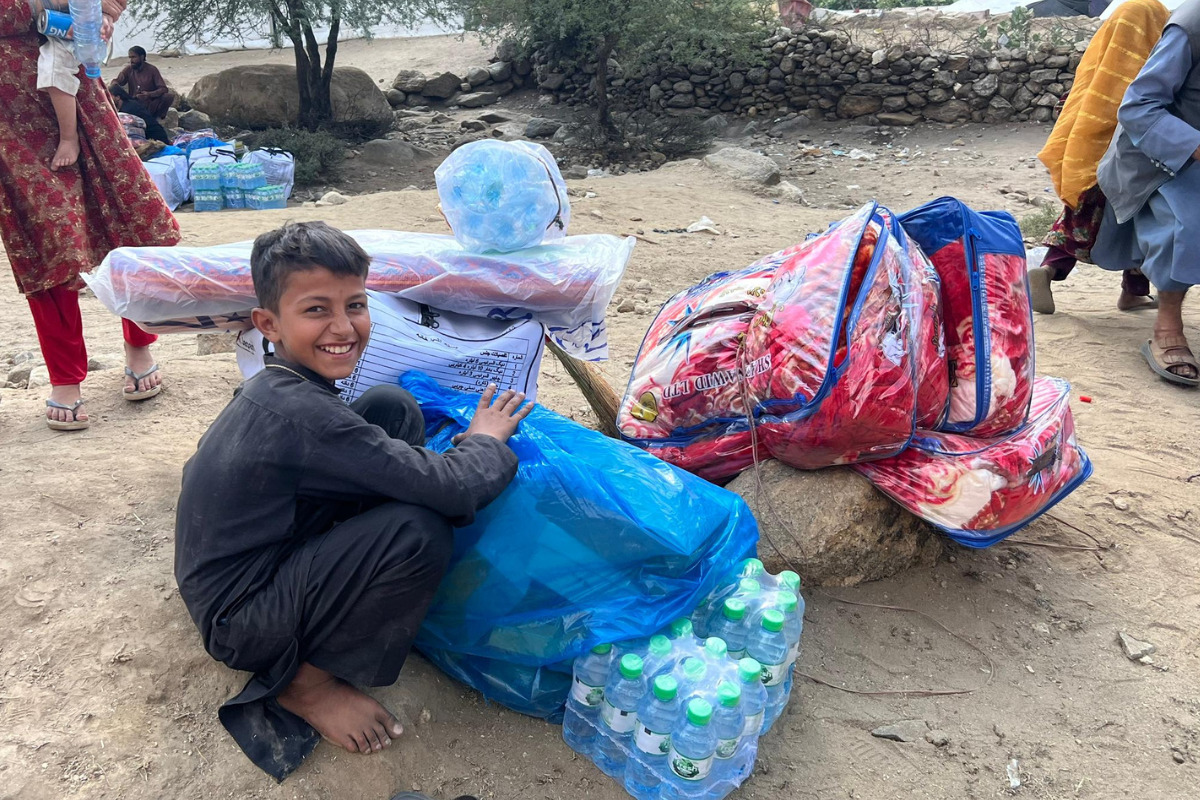 A boy is sitting smiling next to the relief supplies that were distributed by AAR Japan