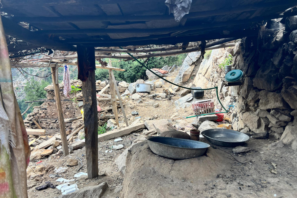 A house has collapsed, leaving only the wooden frame behind. Cooking utensils lie exposed to the elements