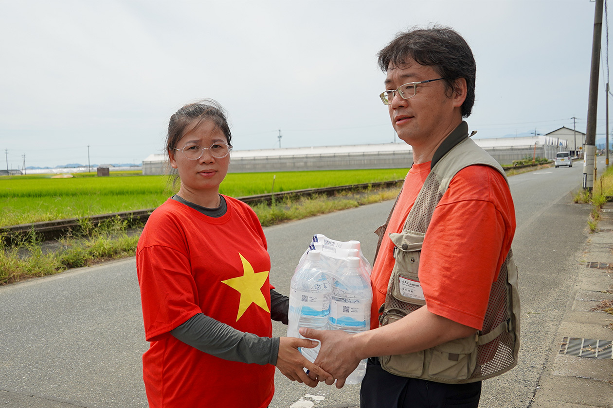A man is handing bottled water to a Vietnamese woman
