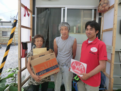 仮設住宅前で支援物資を受け取る方々と難民を助ける会の職員