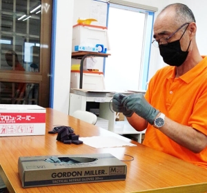 男性が作業台の前でイスに座り、ゴム手袋を着用し、備品の組み立てを行っている