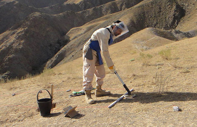 防護服を着て地雷除去の作業を行う男性