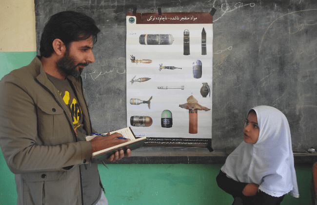 地雷の写真が載っているポスターの写真の前で少女が話している写真