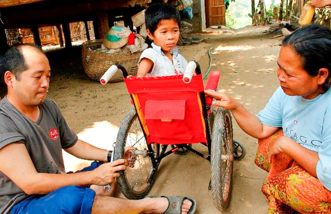 工具を使い男の子が載っている車いすのタイヤを調整するAARスタッフ