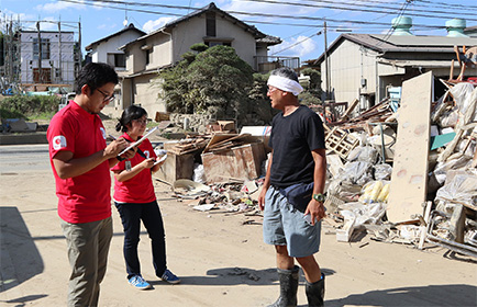 倒壊した家の前で被災者に話を聞くスタッフ２人