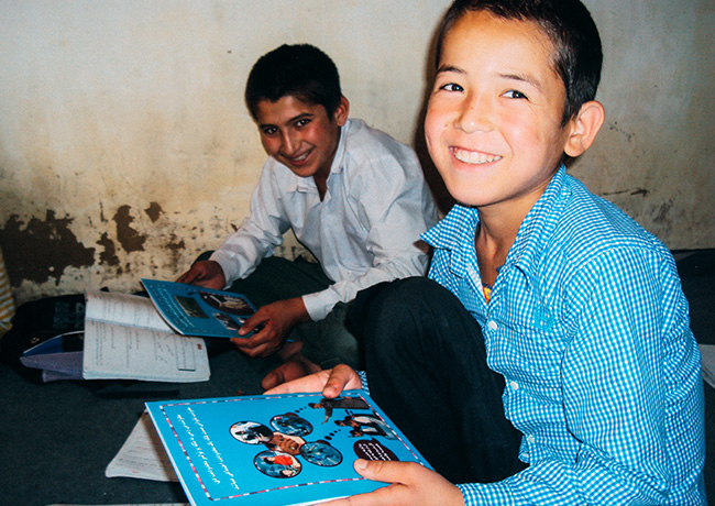 地雷被害を防ぐための方法が掲載されたのノートをうけとり嬉しそうに笑っている男児二人