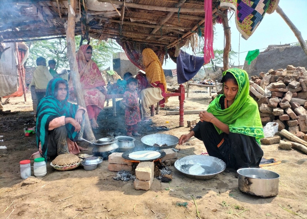 屋外で平たい鍋をレンガを積んだ簡易的なかまどにのせて調理する女性たち