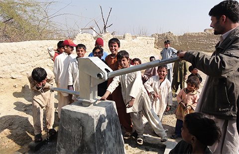井戸から水を汲んでいる男性と、その様子を見ている子供たち