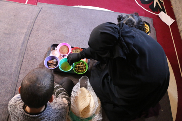 女性が床に座りパンを子どもと食べている写真