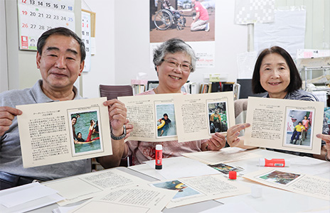 AAR Japanの事務所。ボランティアの男性スタッフ一人と女性スタッフ二人が、ミャンマーの子どもたちの写真と、日本語で書かれた成長記録を手に、微笑んでいる写真