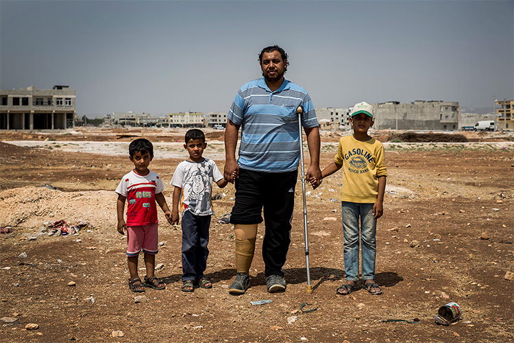 地雷で右足を失ったハーシムさんが3人の子ども達と手をつないで立っている