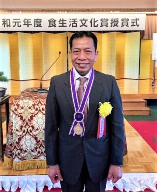 仙田佐武朗さんが食生活文化省の受賞席に出席し、首からメダルを下げて嬉しそうに微笑んでいる