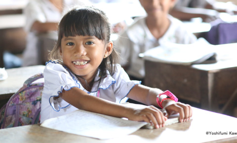 カンボジアの教室の中で、女の子が椅子に座り笑顔でカメラを見ている