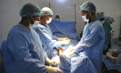 手術室で3人の医師が患者の足のあたりを手術している